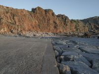 a skateboard parked on a large rocky beach near water at sunrise time with cliff in the background