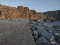 a skateboard parked on a large rocky beach near water at sunrise time with cliff in the background