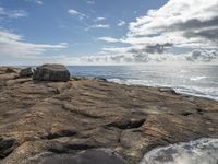 a photo taken by someone looking out over the ocean on rocks in the foreground is water and some sky