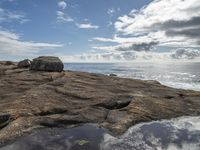 a photo taken by someone looking out over the ocean on rocks in the foreground is water and some sky