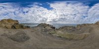 a fish eye lens image of a landscape and rock formations near water and clouds above