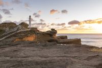 the lighthouse is built near some rocky coastline as the sun sets in the distance above