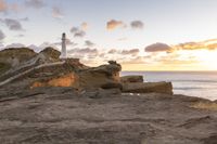 the lighthouse is built near some rocky coastline as the sun sets in the distance above