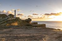 the lighthouse is built near some rocky coastline as the sun sets in the distance above