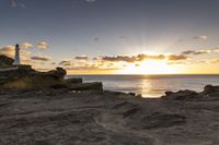 the lighthouse is built near some rocky coastline as the sun sets in the distance above