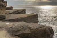 a person stands next to the water looking out to sea, holding a surfboard and standing in front of a rock formation that appears like structure