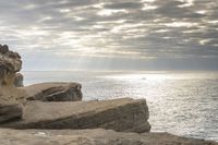 a person stands next to the water looking out to sea, holding a surfboard and standing in front of a rock formation that appears like structure