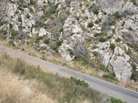 a long road through the mountains with tall grass and rocks along it, with a sign on a stone