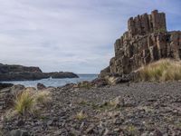 a view from the side of a rocky beach looking towards rocks and water on a cloudy day