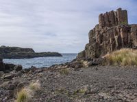 a view from the side of a rocky beach looking towards rocks and water on a cloudy day