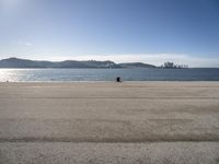 a person sitting on the beach in front of the ocean, looking at the water