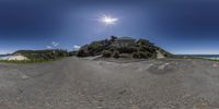 a fish eye view of a house and sand dunes with beach in the background, and bright sunshine streaming through the blue sky