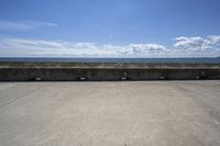 a beach area with concrete wall and ocean in background and sign that says keep off