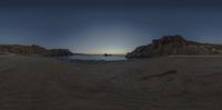 the sun sets on an empty beach with waves crashing toward the rocks, with two small boats out on the water