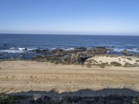 a small rock formation on the beach near the ocean and cliffs, along with an overhang on the shore