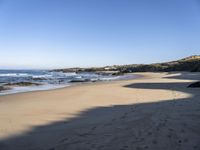 sand covered beach with water and rocks on the edge of the sand dunes and waterline