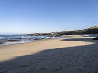 sand covered beach with water and rocks on the edge of the sand dunes and waterline