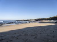 sand covered beach with water and rocks on the edge of the sand dunes and waterline