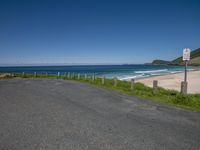 a beach with fence and blue water on a sunny day with no parking sign in foreground