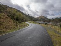 a curved paved road with mountains in the background on a cloudy day near a body of water