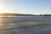 the sun sets behind a wooden fence next to a body of water and mountains behind