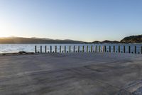 the sun sets behind a wooden fence next to a body of water and mountains behind