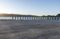 the sun sets behind a wooden fence next to a body of water and mountains behind