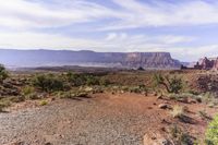 a scenic landscape of red cliffs and sparse grass in desert area with rocks and bushes