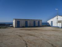 two shed like structures sit along the coastline near the ocean and a small wind vane