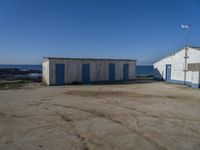 two shed like structures sit along the coastline near the ocean and a small wind vane