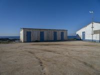 two shed like structures sit along the coastline near the ocean and a small wind vane