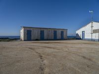 two shed like structures sit along the coastline near the ocean and a small wind vane