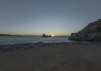 a person sitting on a bench in front of the water at sunset near some rocks