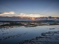 sunset reflects in a beach area with tide covered rocks and small sand areas in the foreground