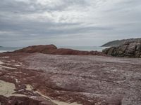 a person with a backpack on a rocky area near the ocean and a hill in the background