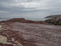 a person with a backpack on a rocky area near the ocean and a hill in the background