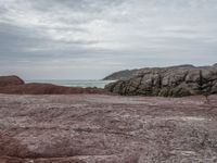 a person with a backpack on a rocky area near the ocean and a hill in the background