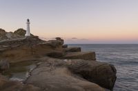 the lighthouse is perched on top of some rocks next to the water and cliffs at sunset