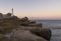 the lighthouse is perched on top of some rocks next to the water and cliffs at sunset