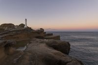 the lighthouse is perched on top of some rocks next to the water and cliffs at sunset