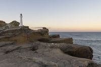 the lighthouse is perched on top of some rocks next to the water and cliffs at sunset