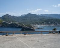 car parked at a bridge overlooking an ocean and mountains of a town with buildings on the sides