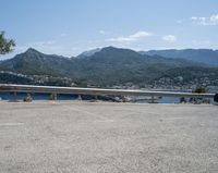 car parked at a bridge overlooking an ocean and mountains of a town with buildings on the sides