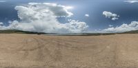 a panoramic photo of a beach with sand and a large cloud over a lake