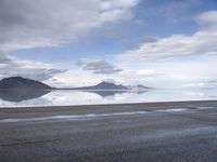 a man is walking along the beach near a large body of water with hills and glaciers