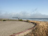 a view of the coast, sand, and ocean, from a path with benches