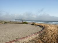 a view of the coast, sand, and ocean, from a path with benches