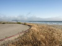 a view of the coast, sand, and ocean, from a path with benches