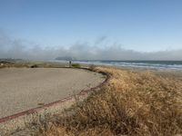 a view of the coast, sand, and ocean, from a path with benches