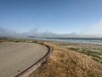 a view of the coast, sand, and ocean, from a path with benches